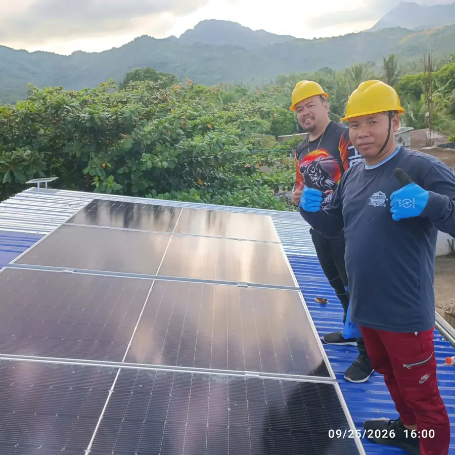 Two MACC installers with thumbs up beside the finished row of solar panels, mountains behind