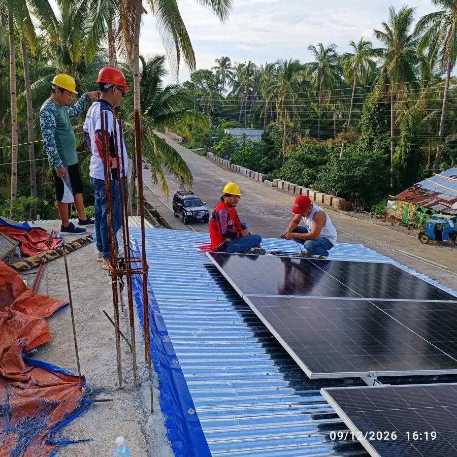 MACC installers fixing solar panels onto a metal roof beside a coconut-lined road